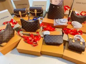 A collection of Louis Vuitton handbags, including different styles, neatly arranged on top of Louis Vuitton packaging boxes, with red ribbons and other accessories around.