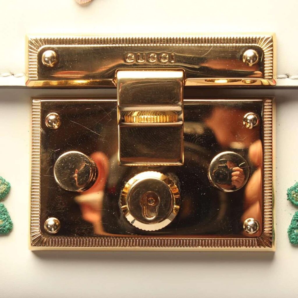 Luxury Bag Craftsmanship-Close-up of Gucci gold-tone hardware lock with engraved brand name and reflective finish.