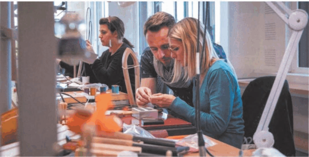 Close-up of artisan hand-stitching waxed linen through layered leather, illustrating Hermès saddle-stitch savoir-faire.