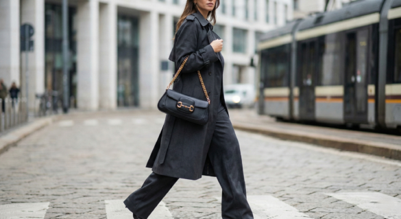 Street style fashion photography featuring one of the Gucci replica bags 2026, the black Horsebit Chain East-West model, worn on the shoulder with a trench coat.